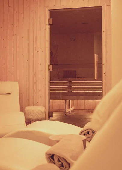 Intérieur de sauna avec chaises longues, serviettes et bancs en bois, éclairé par une lumière chaude à Bois d'Arcy dans les Yvelines 78
