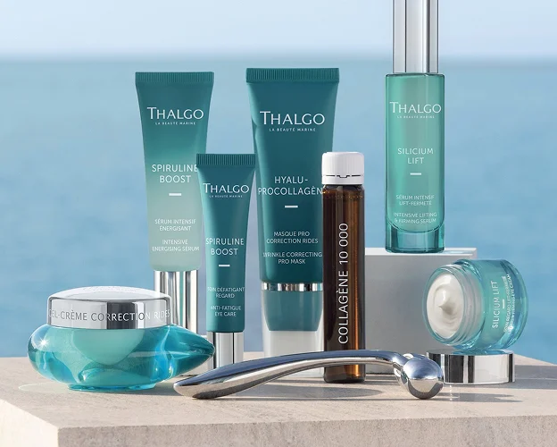 Assortiment de produits de soin Thalgo, bouteilles et pots, sur un fond marin clair.