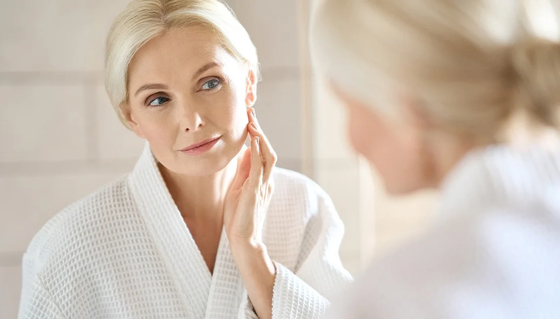 Femme blonde d'âge mûr en peignoir, examinant sa peau dans le miroir à Bois d'Arcy près de Versailles dans les Yvelines 78