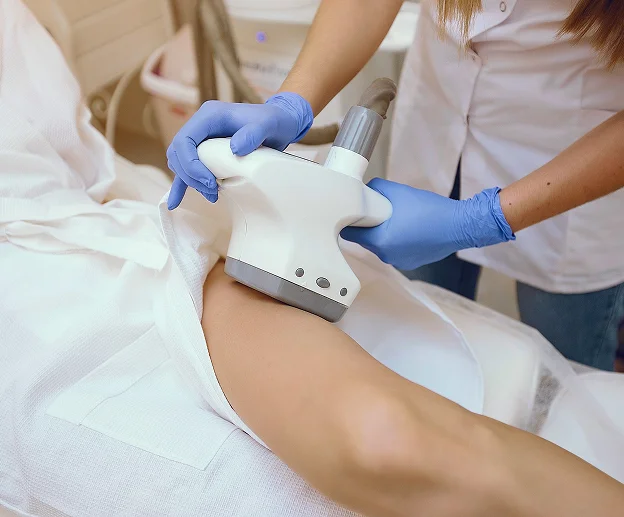 Technicienne gantée effectuant un traitement d'épilation laser sur la jambe d'un client à Bois d'Arcy près de Versailles dans les Yvelines 78
